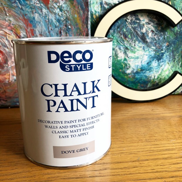tin of Aldi chalk paint on wooden surface with art work behind