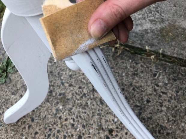 hand holding sandpaper, adding distress to plant stand leg